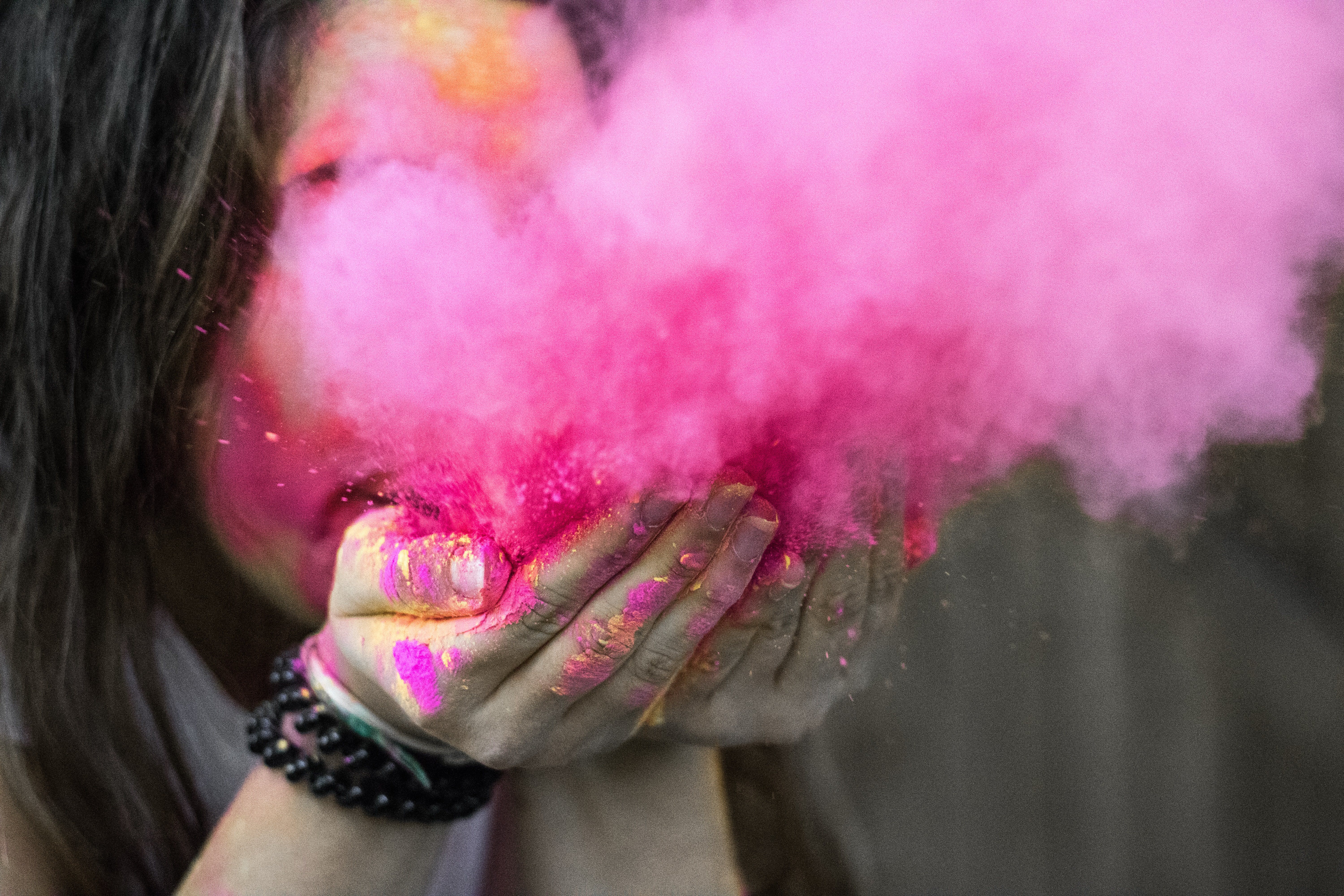 A girl blowing out pink powder so that it creates a pink smoke cloud
