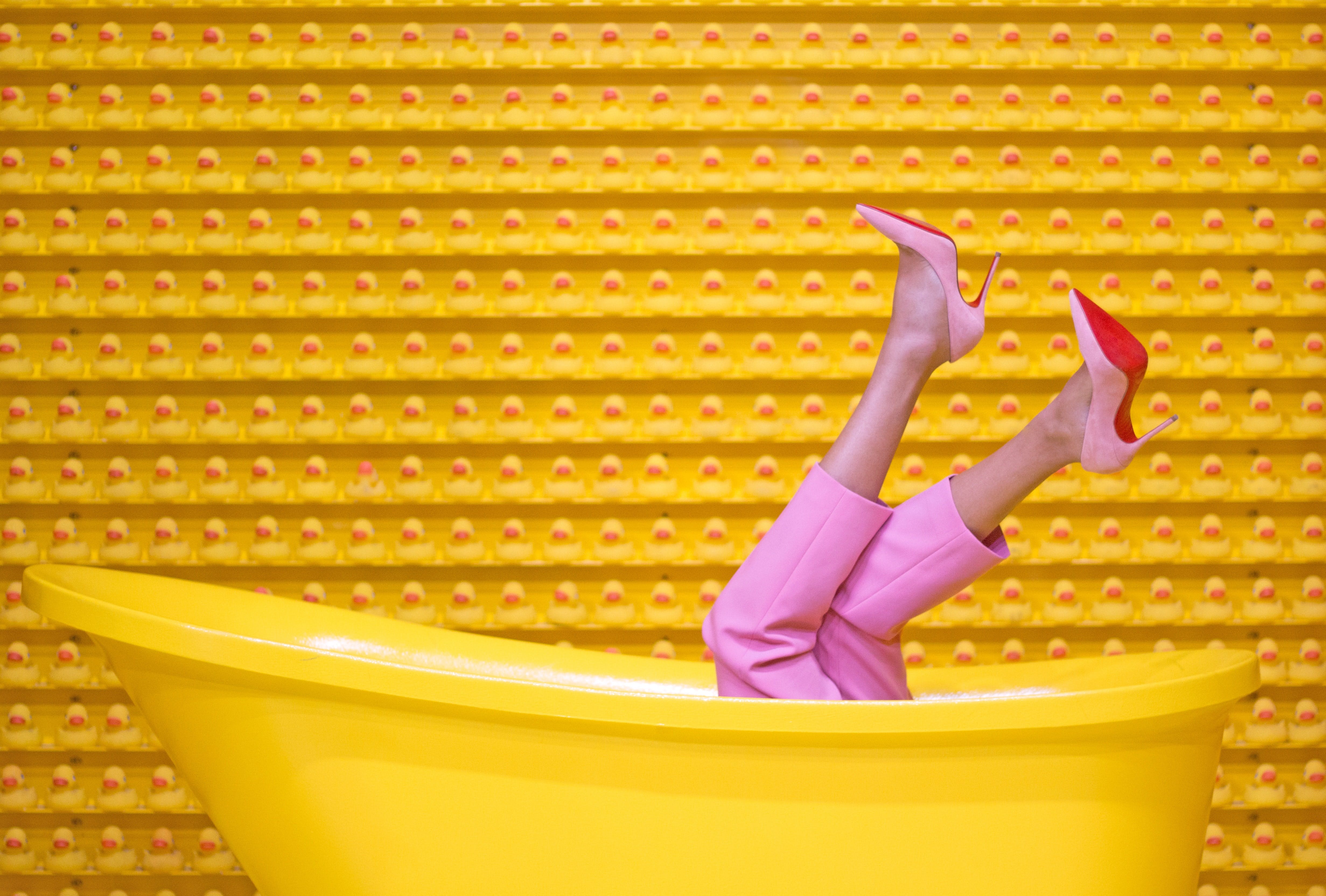 Women in pink clothes sit in a yellow bathtub in front of a yellow wall with red dots