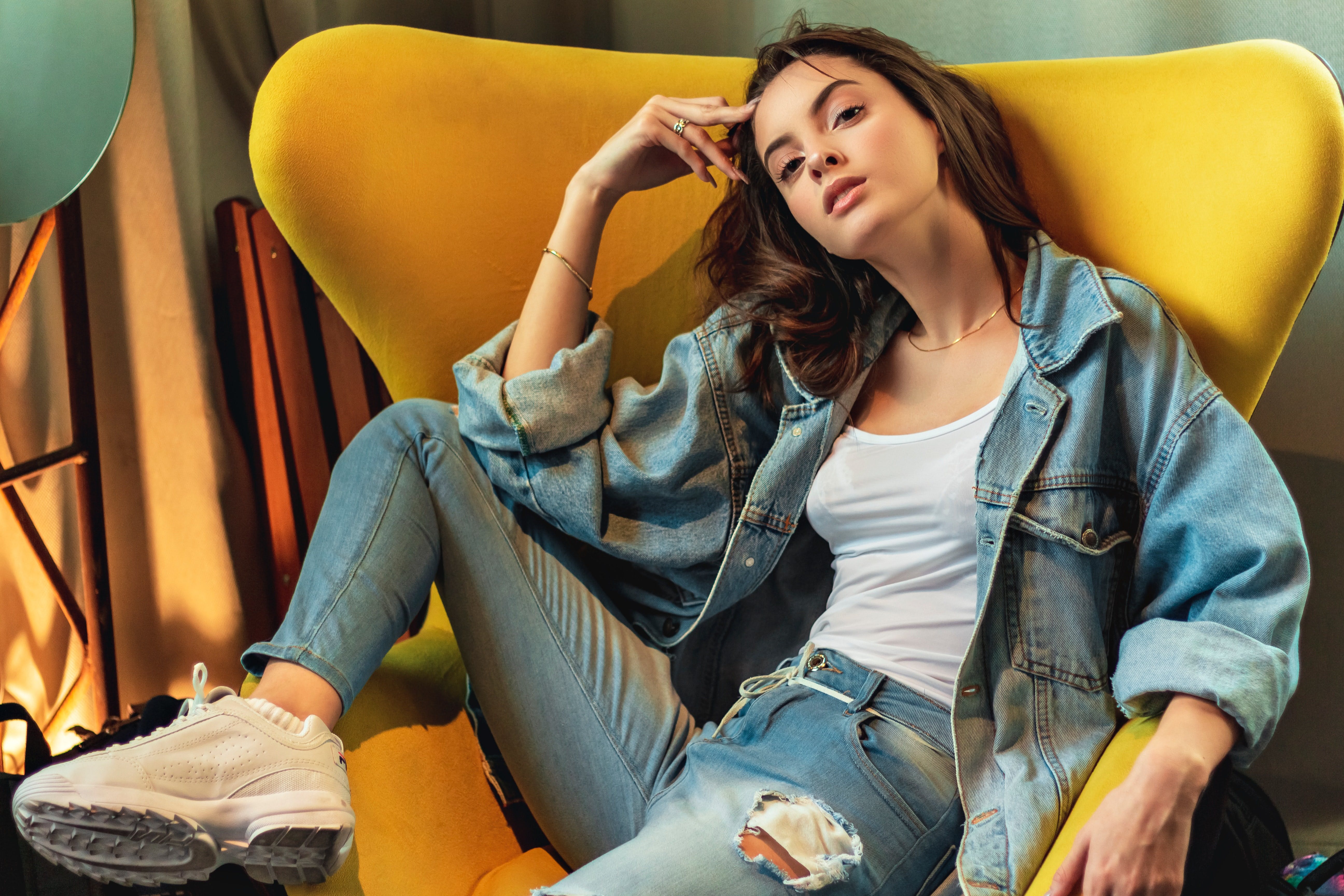 Female brand ambassador in jeans clothes sits in a yellow chair