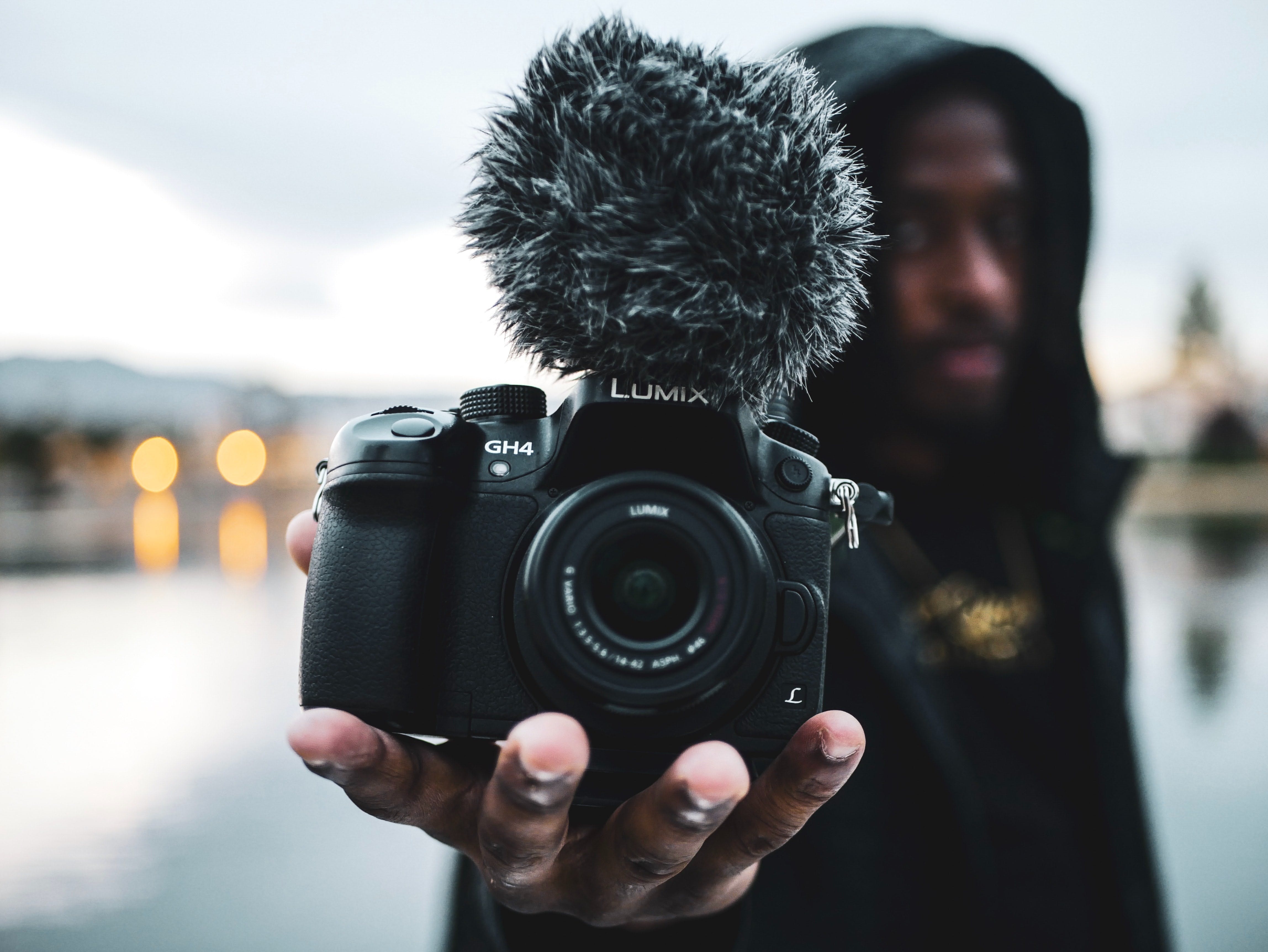 A guy holds a Lumix camera with a mic with a background that is dimmed