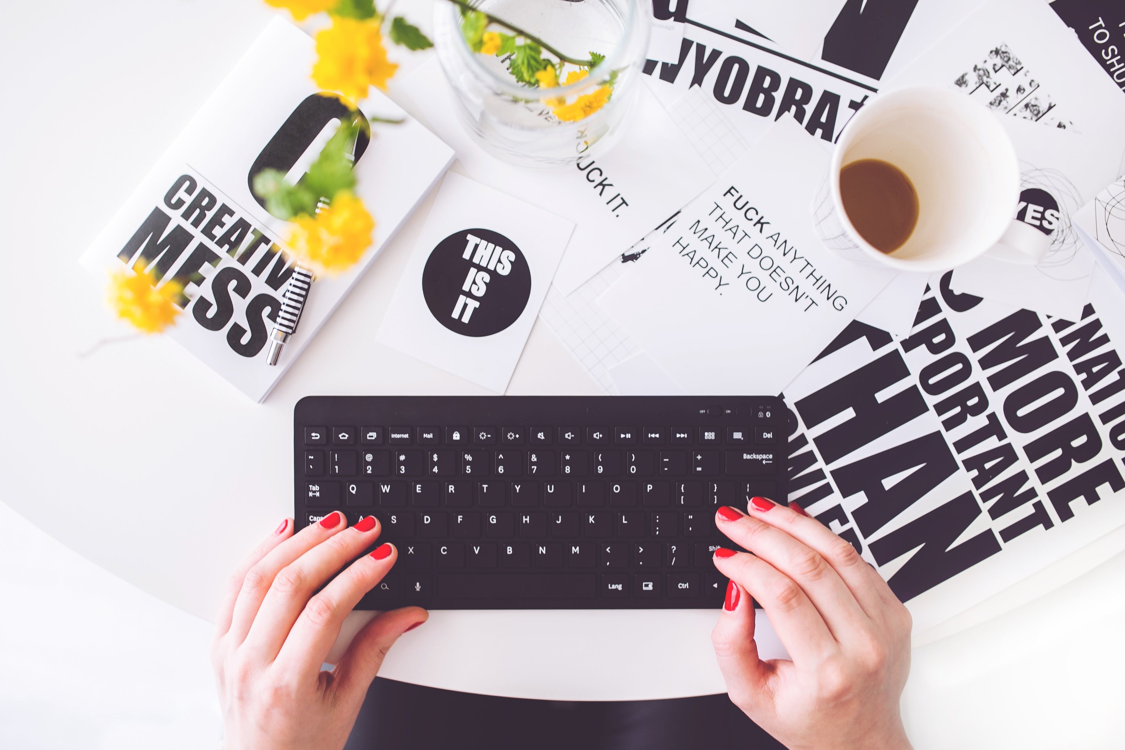 Girl with red nail polishing typing on a keyboard, on a table with a bunch of paper with quotes