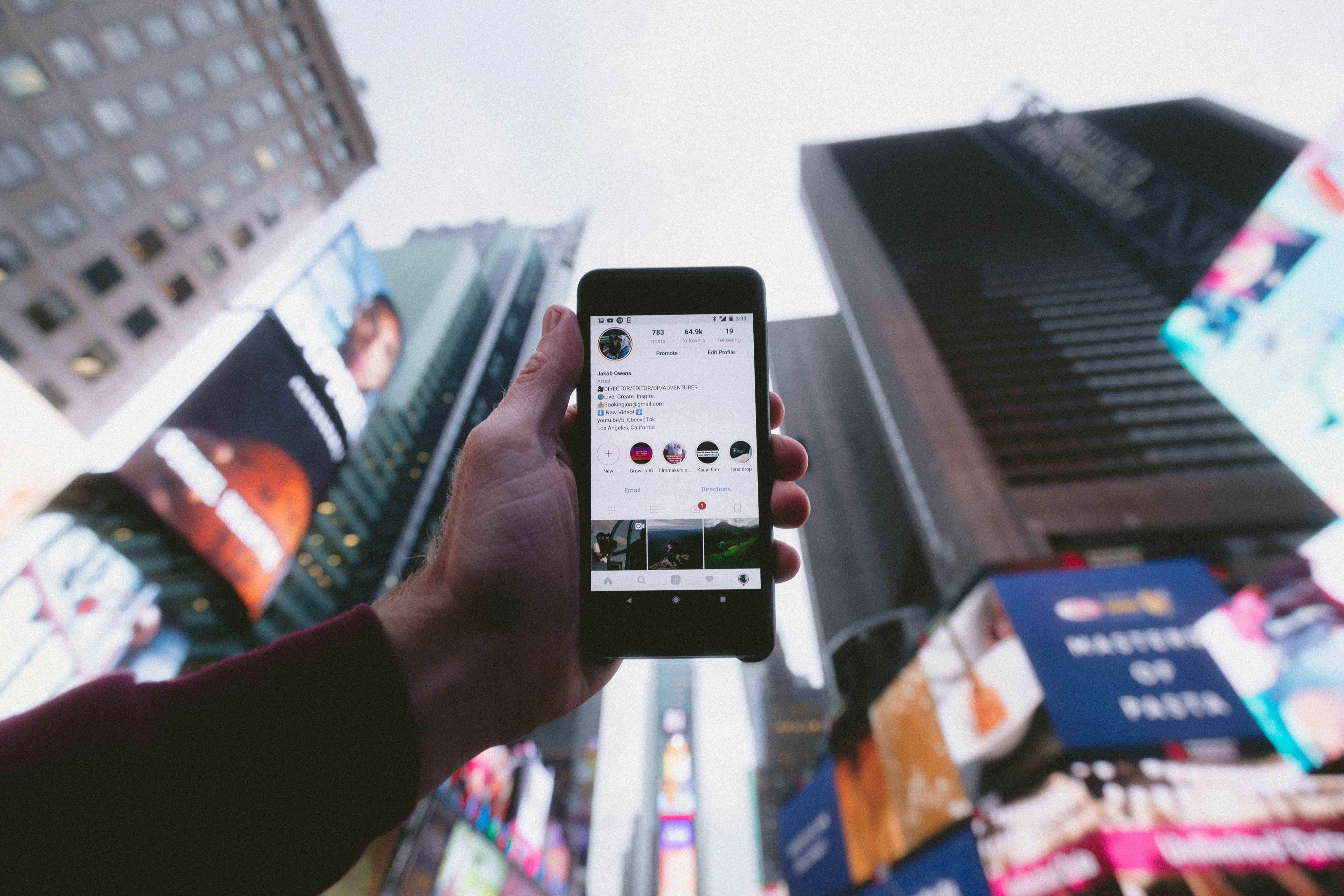 A person holding a phone that shows a instagram account onto the sky in a big city