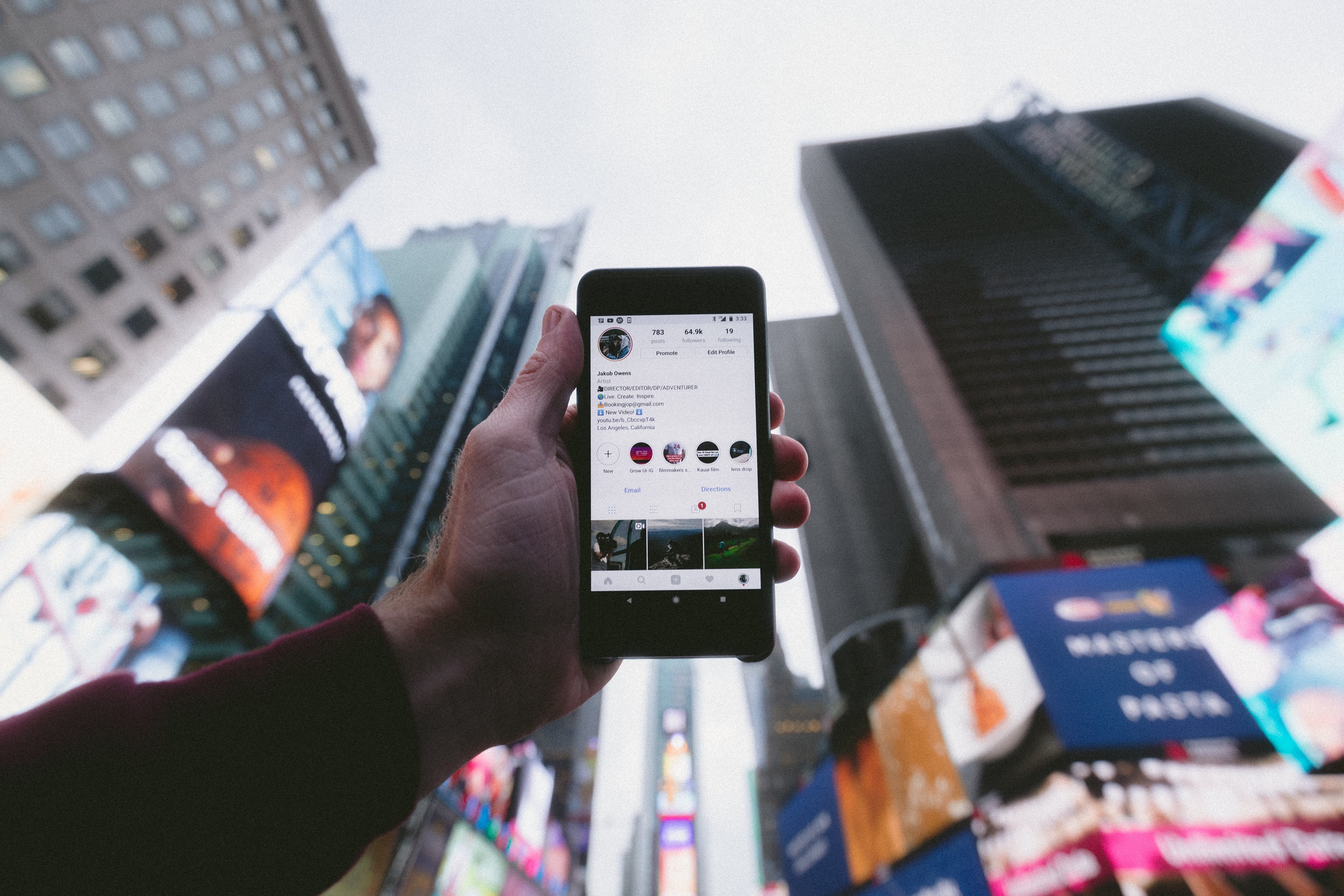 Person som håller i en mobil mot himlen i en storstad och mobilen visar ett instagramkonto