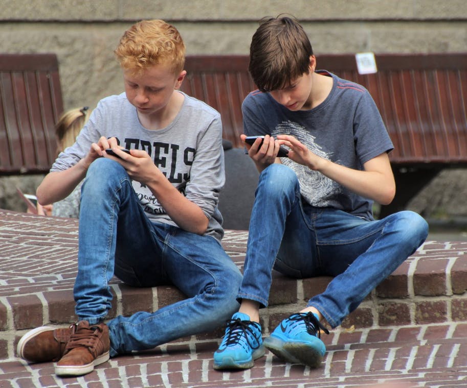 Two teen boys looking at their phones and interacting with it