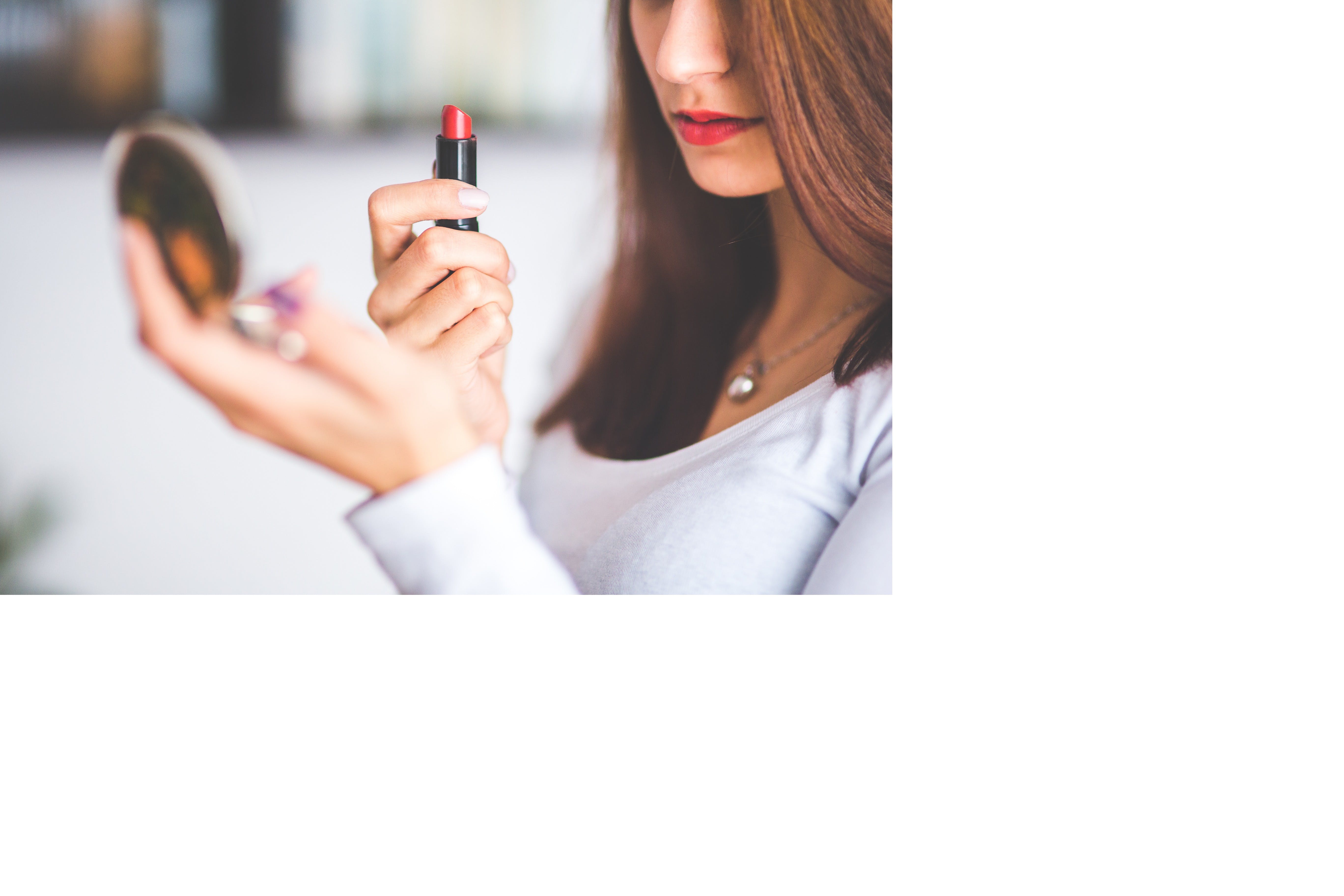 Influencer holding a lipstick and a small mirror trying to fix herself