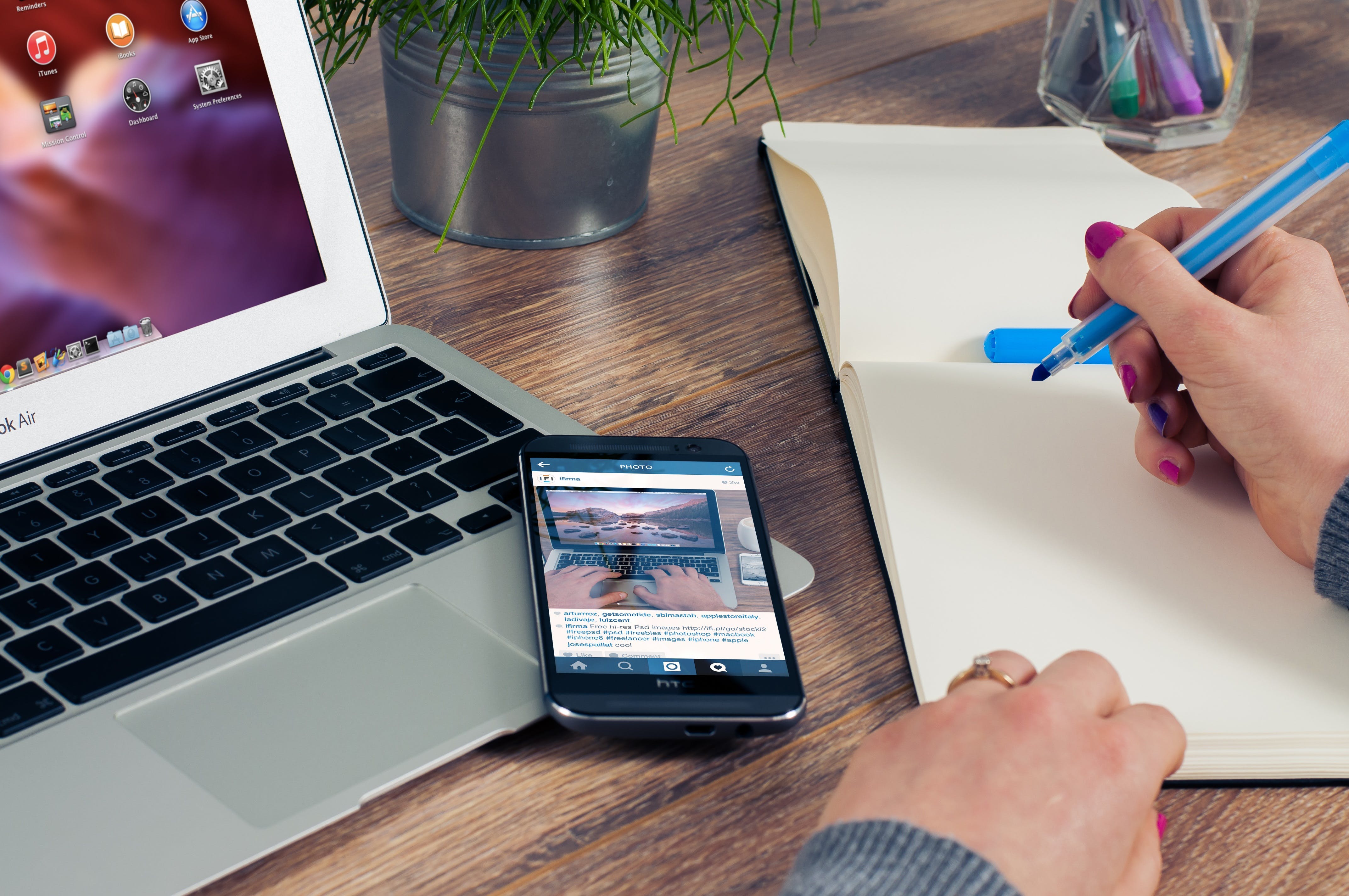 Person sitting at a desk making notes on a pad next to a macbook and phone